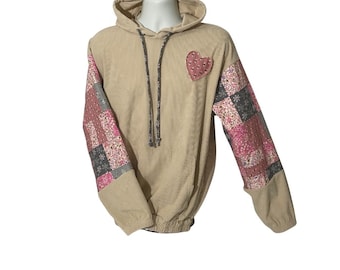 May include: Beige corduroy hoodie with patchwork sleeves in pink, grey, and white floral and geometric patterns. A pink heart applique is on the chest. The hoodie has a drawstring and a hood.