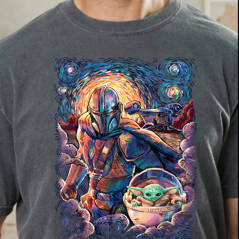 May include: Dark grey crew neck t-shirt with a colourful illustration of a Mandalorian character and Grogu, set against a starry night sky. The artwork includes a spaceship and is rendered in a vibrant, painterly style.