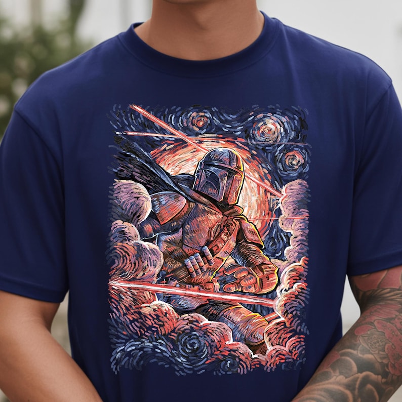 May include: Navy blue t-shirt featuring a stylized illustration of The Mandalorian in a starry night setting. The artwork depicts the character amidst red laser blasts and swirling clouds, with a helmet and armor.