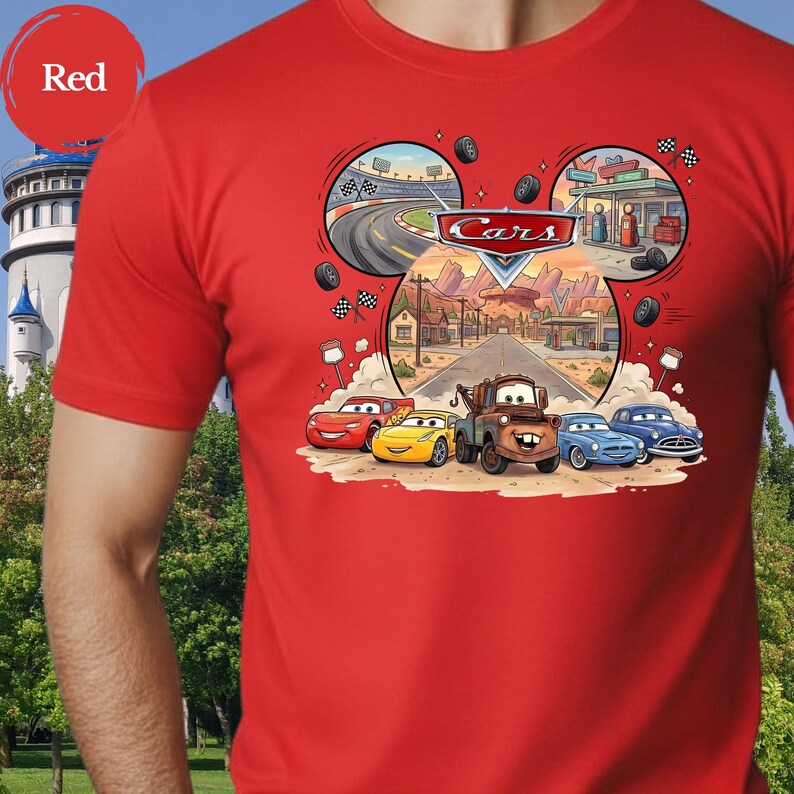Pode incluir: Uma t-shirt vermelha brilhante com uma impress&atilde;o gr&aacute;fica das personagens do filme Carros, incluindo Rel&acirc;mpago McQueen e Mate. O design tem a forma de uma cabe&ccedil;a do Mickey Mouse e incorpora cenas de uma pista de corridas e paisagens des&eacute;rticas.