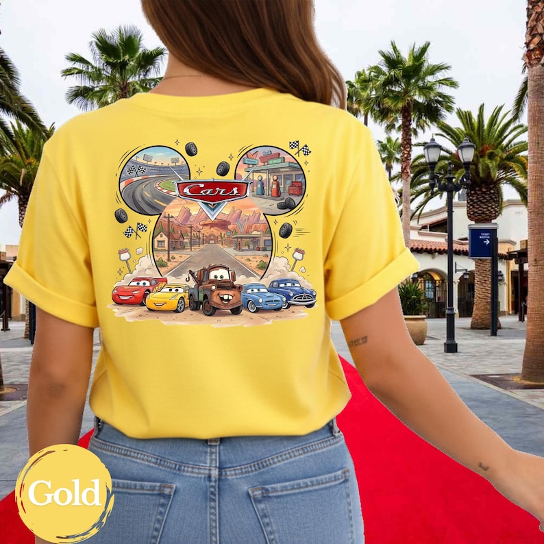 Pu&ograve; includere: Una t-shirt giallo brillante con una grafica sul retro che mostra il logo Disney Cars e personaggi come Saetta McQueen e Cricchetto. Il design include una pista da corsa, un paesaggio desertico e vari elementi a tema automobilistico.