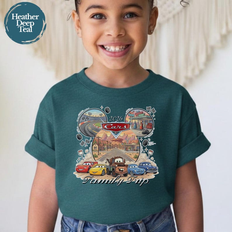 Puede incluir: Una camiseta verde azulado con un gr&aacute;fico de los personajes de la pel&iacute;cula Cars en forma de cabeza de Mickey Mouse. El dise&ntilde;o incluye el texto "2026 Cars Family Trip" e im&aacute;genes de pistas de carreras y una gasolinera.
