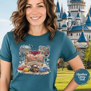 Puede incluir: Camiseta de color verde azulado con un dise&ntilde;o gr&aacute;fico de los personajes de Cars y una escena de viaje. El dise&ntilde;o incluye el texto "2026 Cars Family Trip" en forma de oreja de Mickey Mouse. La camiseta es de color verde azulado jaspeado.
