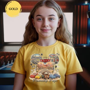 Puede incluir: Una camiseta amarilla con un gr&aacute;fico de los personajes de Cars de Disney y el texto "Family Trip". El dise&ntilde;o incluye im&aacute;genes de coches de carreras, una gasolinera y el texto "2020 Cars".