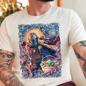 May include: Off-white t-shirt with a colourful illustration of The Mandalorian and Grogu, set against a swirling, starry night sky. The artwork showcases the characters in a vibrant, artistic style, with a spaceship in the background. A unique graphic tee.