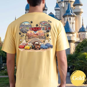 Pu&ograve; includere: Una t-shirt giallo pallido con una grafica sul retro che mostra il logo Disney Cars e personaggi tra cui Saetta McQueen, Cricchetto e altri. Il disegno &egrave; incorniciato in una silhouette a orecchie di Topolino con pista e citt&agrave;.