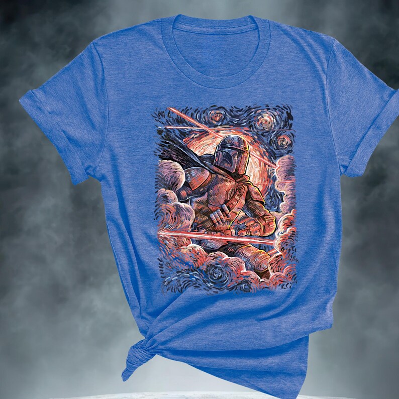 May include: Blue t-shirt featuring a graphic of a character in armor, set against a starry night sky with red laser beams. The artwork has a painterly style, with a color palette of blues, reds, and oranges.