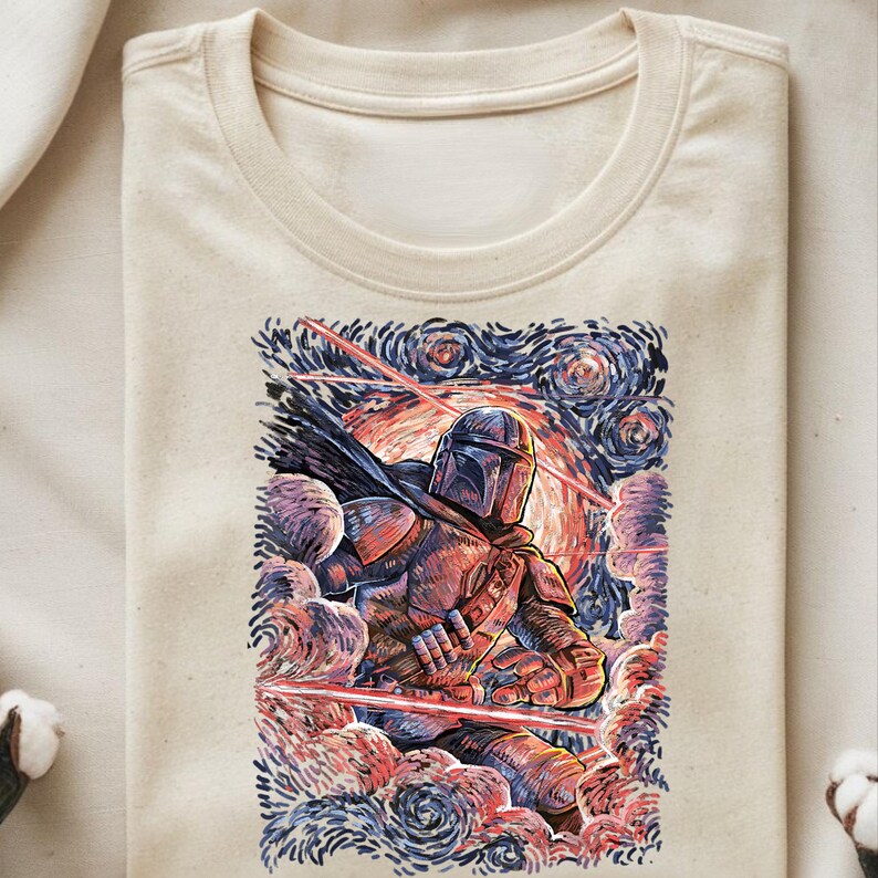 May include: Beige crew neck t-shirt featuring a colorful illustration of a Mandalorian warrior in a starry night style. The artwork includes red laser beams and swirling clouds in shades of blue, red, and purple.