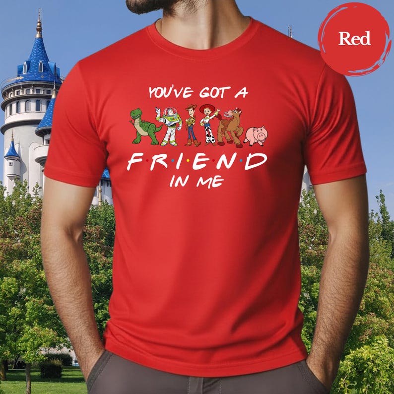 May include: A red t-shirt featuring the phrase "YOU'VE GOT A FRIEND IN ME" with cartoon character graphics. The design includes a green dinosaur, a space ranger, a cowboy, a cowgirl, a horse, and a pig.