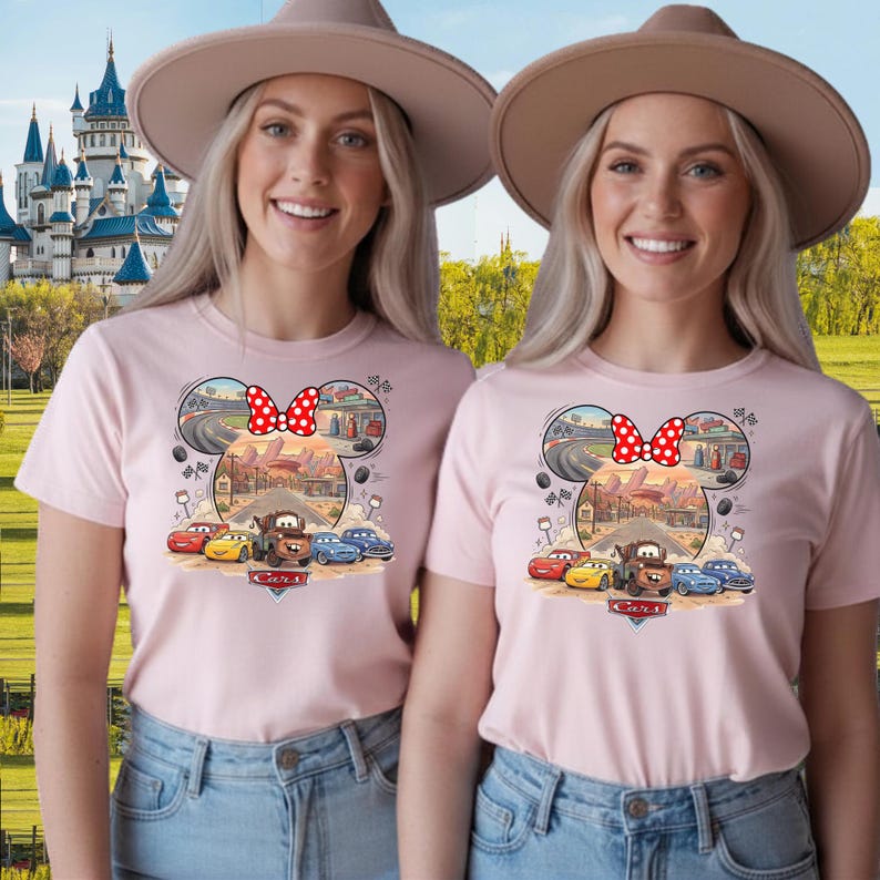 Pode incluir: Uma t-shirt rosa claro com um gr&aacute;fico das personagens do filme Carros da Disney Pixar, incluindo o Fa&iacute;sca McQueen e o Mate. O design tem a forma de uma cabe&ccedil;a do Rato Mickey com um la&ccedil;o vermelho de bolinhas brancas e o log&oacute;tipo Cars.