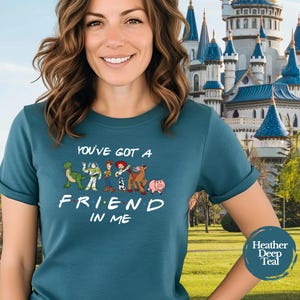 May include: Teal t-shirt featuring the phrase "You've Got a Friend in Me" with cartoon characters. The shirt has a crew neck and short sleeves. The background shows a castle and a blue circle with the words "Heather Deep Teal".