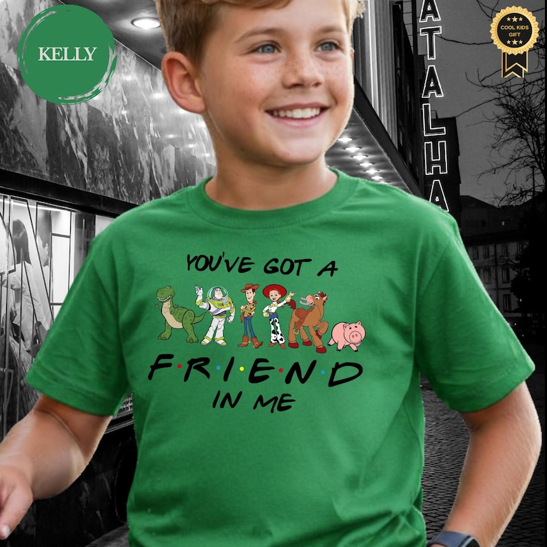 May include: A green t-shirt featuring the phrase "You've Got A Friend In Me" with cartoon character graphics. The shirt has a crew neck and short sleeves. The design includes a dinosaur, Buzz Lightyear, Woody, Jessie, a horse, and a pig.