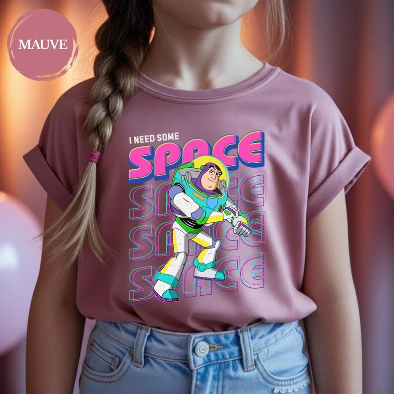 May include: Mauve-colored t-shirt featuring Buzz Lightyear from Toy Story. The graphic includes the text "I NEED SOME SPACE" in a colorful, retro font. Buzz Lightyear is depicted in his signature space suit. The shirt is made of soft material.