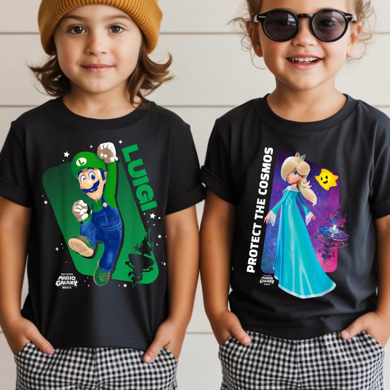 May include: Two children wearing black t-shirts. One shirt features Luigi from Mario Galaxy, the other features Princess Rosalina with the text "Protect the Cosmos". Both shirts have the Mario Galaxy logo.