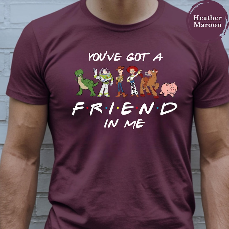May include: Heather maroon t-shirt featuring the phrase "You've Got a Friend in Me" with cartoon characters from the movie Toy Story. The characters include a dinosaur, Buzz Lightyear, Woody, Jessie, Bullseye, and Hamm.