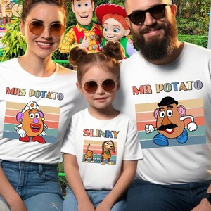 May include: Three white t-shirts featuring retro-style graphic prints of characters. One shirt displays Mrs. Potato with the text "MRS POTATO", one shows Slinky with the text "SLINKY", and one features Mr. Potato with the text "MR POTATO".
