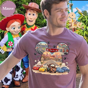Pode incluir: Uma t-shirt de manga curta cor de malva com um gr&aacute;fico das personagens Disney Pixar Cars, incluindo Rel&acirc;mpago McQueen, Mate e outros. O design inclui uma moldura em forma de orelhas do Mickey com cenas de uma pista e Radiator Springs.