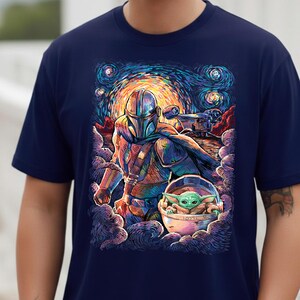 May include: Navy blue t-shirt with a colourful illustration of The Mandalorian, Grogu, and a spaceship set against a starry night sky. The artwork has a painterly style with vibrant blues, oranges, and greens.