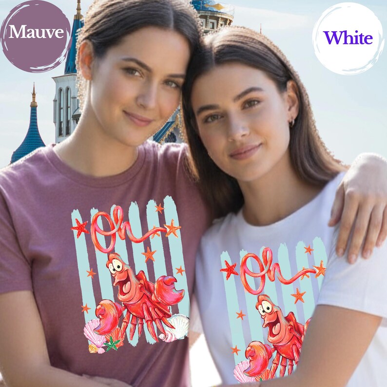 Pu&ograve; includere: Una t-shirt color malva e una t-shirt bianca, entrambe con una stampa grafica di un granchio rosso dagli occhi grandi, la parola "Oh" in corsivo rosso, strisce verticali azzurre, piccole stelle marine arancioni e conchiglie.