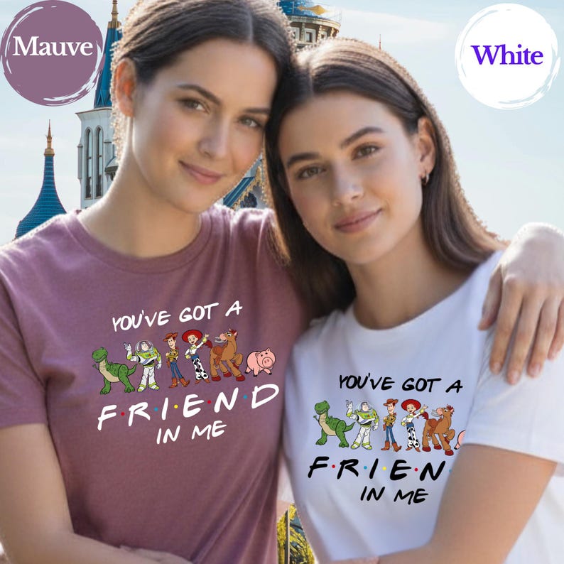 May include: Two women wearing matching t-shirts. One shirt is mauve, the other is white. Both shirts feature the phrase "YOU'VE GOT A FRIEND IN ME" with cartoon character graphics. The background includes a castle.