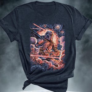 May include: Dark navy blue t-shirt featuring a colorful illustration of a character in armor, set against a swirling, starry background with red laser beams. The artwork evokes a blend of science fiction and classic art styles.