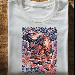 May include: White t-shirt featuring a colorful illustration of a character in armor, set against a swirling, starry night sky. The artwork incorporates shades of blue, red, and orange, creating a dynamic and artistic design.