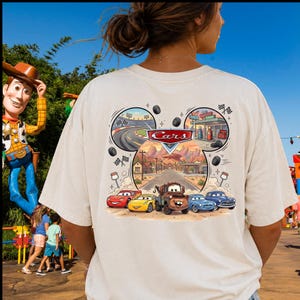 Pu&ograve; includere: Una t-shirt a maniche corte color crema con una grafica sul retro che include il logo Disney Pixar Cars. Il design presenta una cornice a forma di testa di Topolino contenente un circuito, una stazione di servizio e i personaggi Saetta McQueen e Cricchetto.