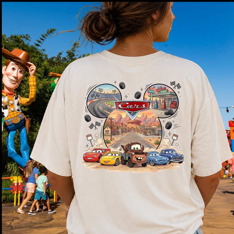 Pu&ograve; includere: Una t-shirt a maniche corte color crema con una grafica sul retro che include il logo Disney Pixar Cars. Il design presenta una cornice a forma di testa di Topolino contenente un circuito, una stazione di servizio e i personaggi Saetta McQueen e Cricchetto.