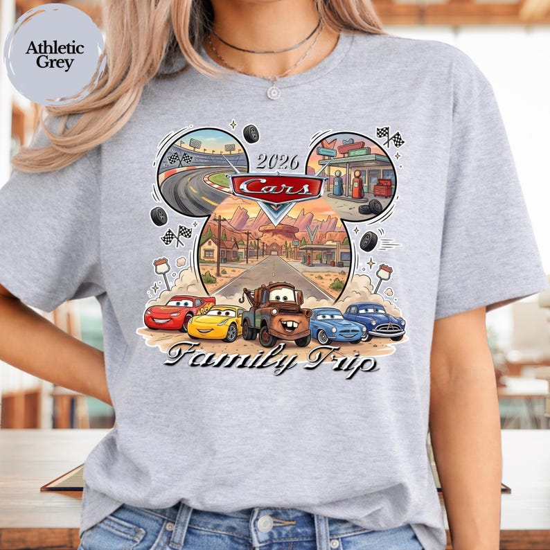 Puede incluir: Camiseta gris deportivo con un gr&aacute;fico colorido de Cars. El dise&ntilde;o presenta personajes de Cars, una carretera des&eacute;rtica y el texto "2026 Cars Family Trip". La camiseta es de material suave.