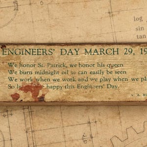 May include: A rectangular wooden plaque featuring the text ENGINEERS' DAY MARCH 29, 1923, along with a poem about St. Patrick and engineering. The plaque includes green printed illustrations of a tripod, a gear, and a building, with a weathered finish.