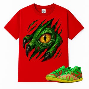 以下が含まれることがあります： 鮮やかな赤の半袖Tシャツで、引き裂かれた布地から現れる緑色の爬虫類の目と爪のグラフィックが描かれています。Tシャツの下には、黄色のソールとテクスチャパターンを持つ緑と赤のスポーツシューズが配置されています。