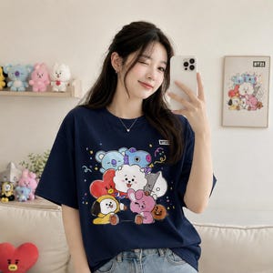 May include: Navy blue t-shirt featuring a colorful graphic of BT21 characters. The design includes cartoon figures in various colors, such as blue, pink, and yellow. The shirt has short sleeves and a crew neck.