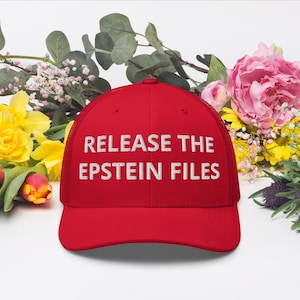 May include: A red trucker hat with the phrase "RELEASE THE EPSTEIN FILES" embroidered in white. The hat is set against a backdrop of colorful flowers, including yellow daffodils and pink peonies.