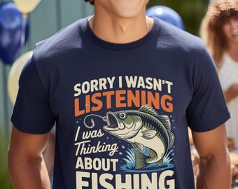 May include: Navy blue t-shirt with the text "SORRY I WASN'T LISTENING I was Thinking ABOUT FISHING" and a graphic of a fish jumping out of the water. The shirt is a casual wear item.