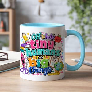 May include: A white ceramic mug with a light blue handle and interior rim. The mug features a colorful graphic with school supplies and the text "Off to help tiny humans do big things" in various fonts, colors, and styles, including a pencil, books, and globe.