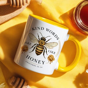 May include: White ceramic mug with a yellow handle and interior. The mug features a detailed illustration of a bee with the words "Kind Words Are Like Honey" and the Bible verse Proverbs 16:24.