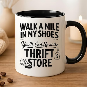 May include: White ceramic mug with a black interior and handle. The mug features the text "WALK A MILE IN MY SHOES You'll End Up at the THRIFT STORE" in black, along with a shoe graphic and a price tag icon.