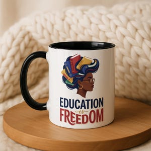 White mug with black rim and handle, featuring graphic of woman with books in hair and text "Education is Freedom".