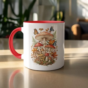 May include: White ceramic mug with a red handle and rim. The mug features a detailed illustration of various mushrooms, autumn leaves, and butterflies. The design includes shades of brown, red, and orange.