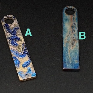 May include: Two rectangular pendants with a hole at the top. One pendant has a blue and gold marbled design, labeled "A". The other pendant, labeled "B", has a blue and rust-colored marbled design. Both pendants are on a black surface.