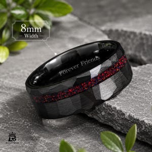 Könnte beinhalten: Ein schwarzer Ring mit gehämmertem Muster und einer Breite von 8 mm. Das Band verfügt über eine mittige Einlage aus rotem Opal-Splitter und den eingravierten Text Forever Friends auf der Innenseite. Der Ring hat eine polierte Innenseite.