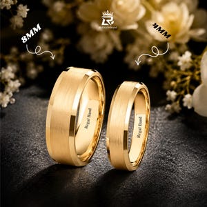 Puede incluir: Dos anillos de color dorado con acabado cepillado y bordes biselados pulidos. El anillo más grande está marcado como 8mm y el más pequeño como 4mm. Ambos anillos tienen grabado el texto Regal Band en la superficie interior, con un logo arriba.