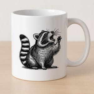 Puede incluir: Taza de cer&aacute;mica blanca con una ilustraci&oacute;n en blanco y negro de un mapache, con la boca abierta y una pata levantada. El mapache tiene una cola rayada. La taza tiene un asa curva.