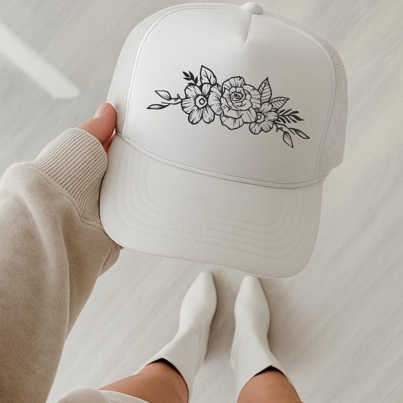 Pu&ograve; includere: Cappellino da camionista bianco con design floreale. Il cappellino ha un pannello frontale bianco e un retro in rete. Un design floreale nero, tra cui rose e foglie, &egrave; centrato sulla parte anteriore.