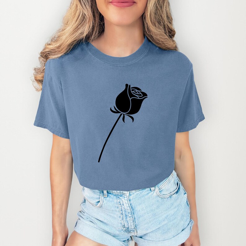 Pu&ograve; includere: Una maglietta blu con un disegno di rosa nera. La rosa &egrave; raffigurata con un bocciolo dettagliato e un lungo stelo. Il colore pieno della maglietta offre uno sfondo chiaro per la grafica floreale. La maglietta &egrave; realizzata in un materiale morbido.