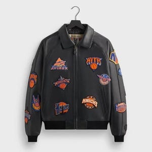 May include: Black leather jacket with multiple patches featuring basketball-related logos and text. The jacket has a zip-up front, a collar, and ribbed cuffs and hem. Patches include the text "Knicks" and "Kith".