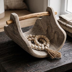 May include: A wooden decorative tray with a natural finish. The tray has a handle made of a small branch and holds a beaded necklace with a tassel. The tray is on a dark wooden surface.