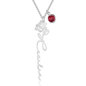 May include: A silver-toned necklace featuring a vertical pendant with a script name Cecilia and a floral design at the top. A small, round, faceted red gemstone charm hangs from the chain next to the main pendant on a delicate silver link chain.