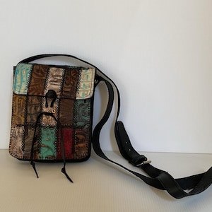 May include: A patchwork crossbody bag with a black strap. The bag features a variety of textured leather patches in shades of brown, teal, and red. The bag has a flap closure with a black leather tie.