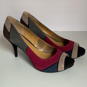 May include: A pair of high-heeled peep-toe pumps. The shoes feature a color-block design with panels of brown, gray, burgundy, tan, and navy blue suede. The heels are black and the insoles are tan.